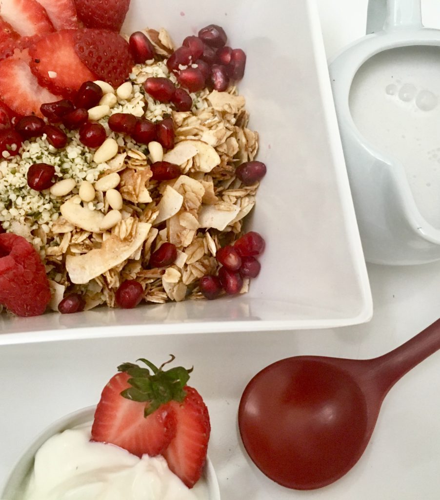 Coconut-Almond Cereal with Strawberries Raspberries in a white bowl yoghurt, and cocnut milk with a red lacquer spoon